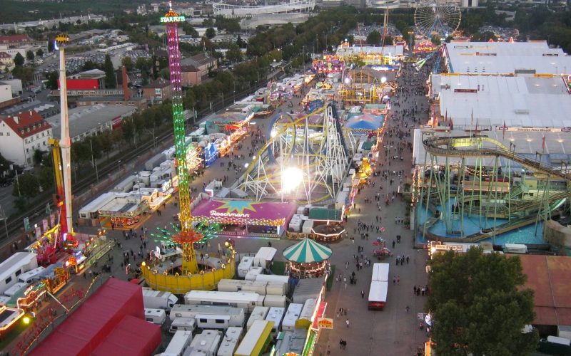 Aerial view of the Cannstatter Volksfest fairground at dusk with rides and beer tents