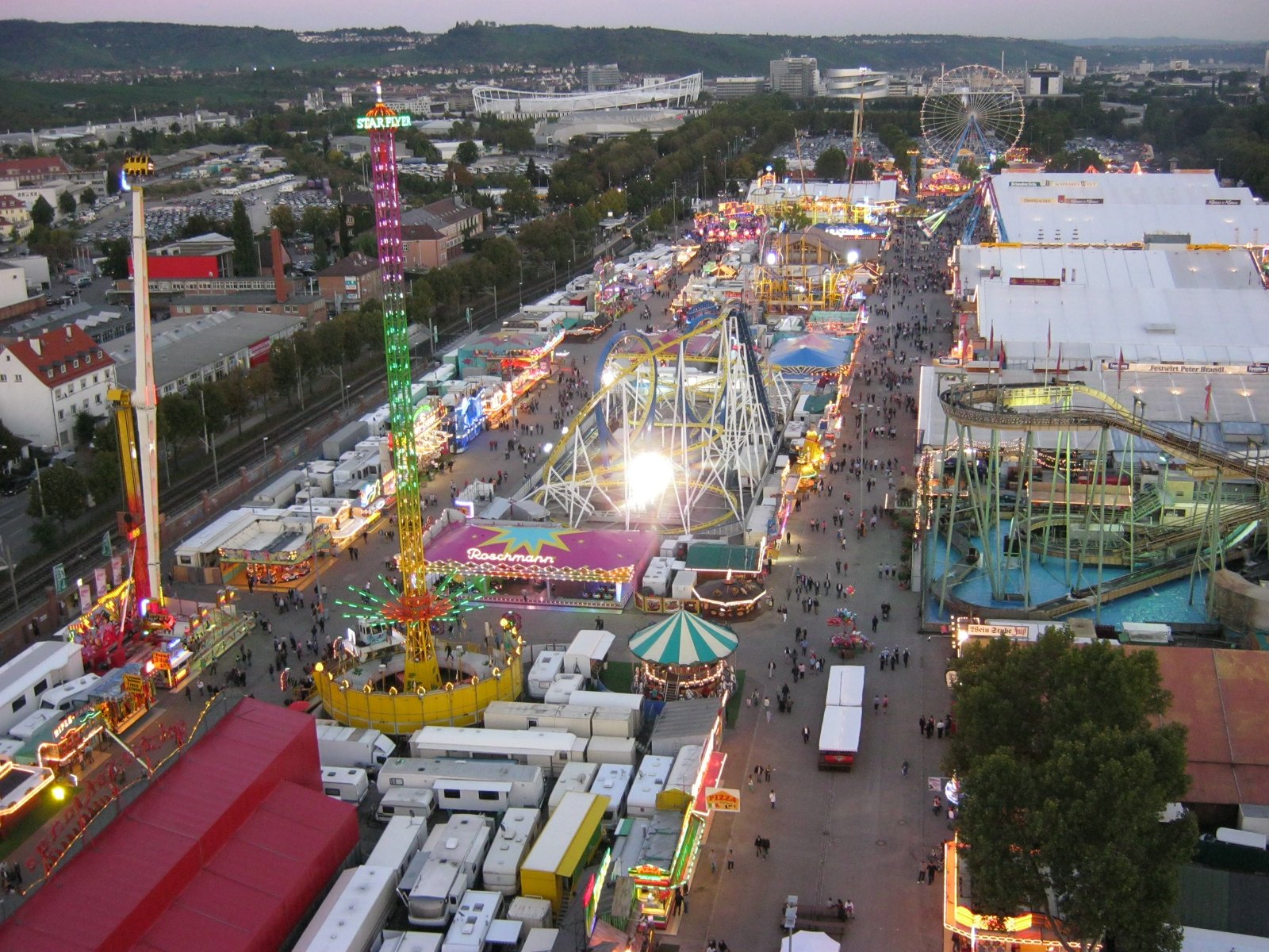 Aerial view of the Cannstatter Volksfest fairground at dusk with rides and beer tents