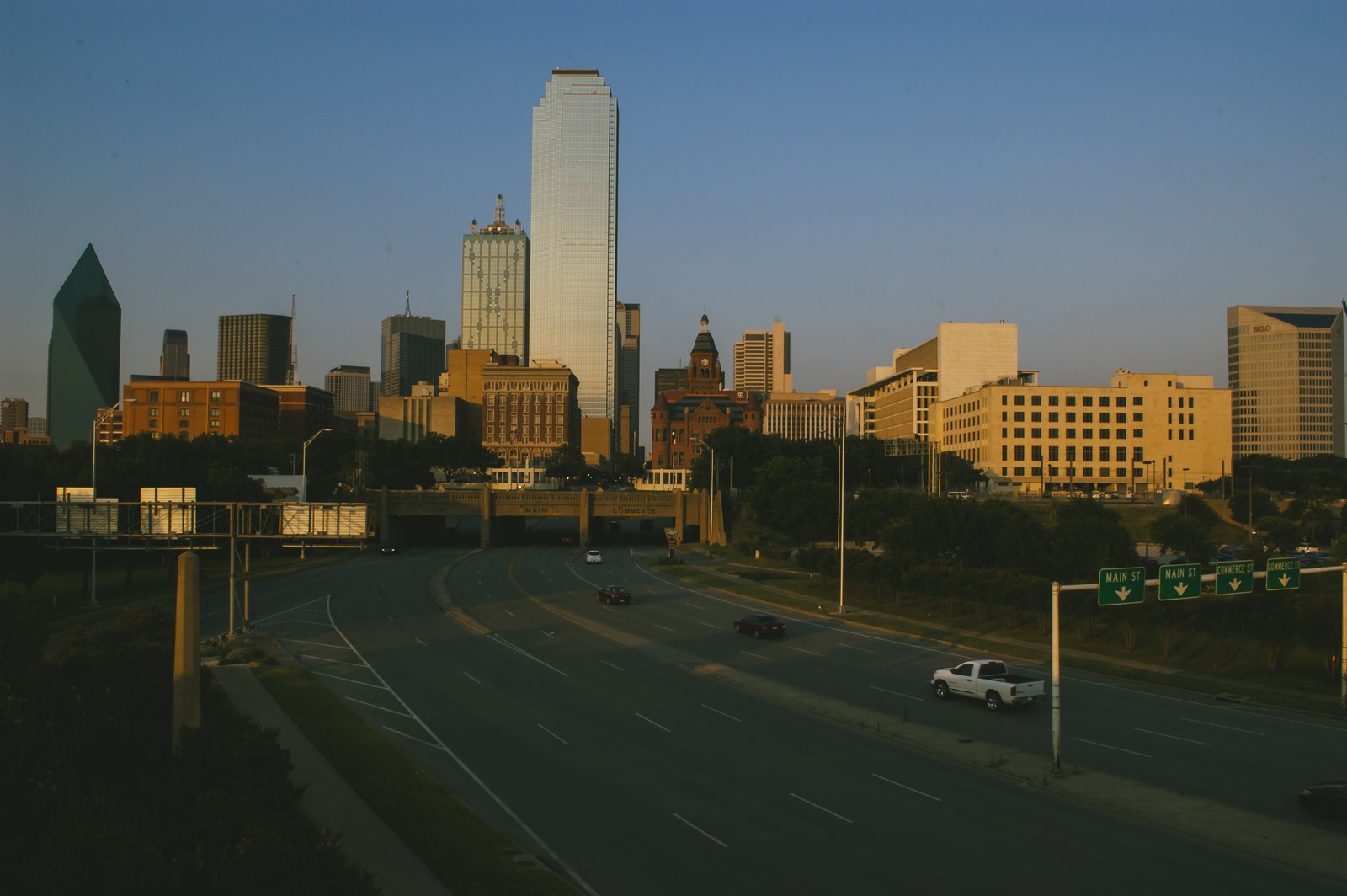 Dallas towers lit by evening sun above a downtown highway