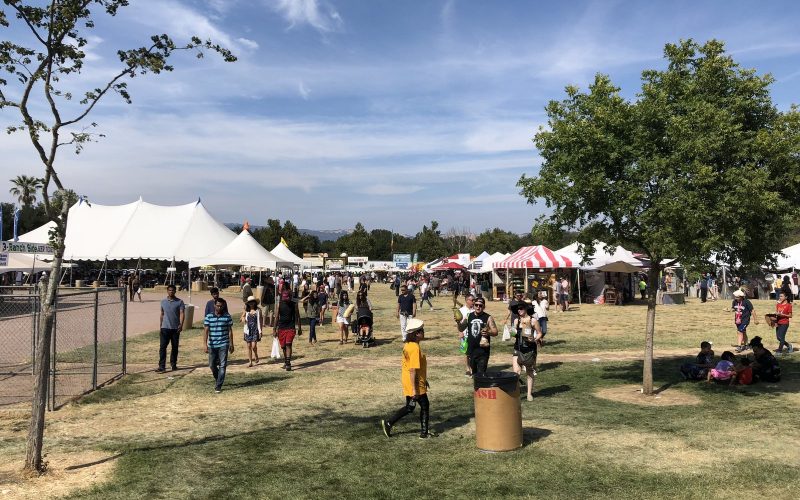 Visitors walking across the sunny Gilroy Garlic Festival grounds with white tents under blue sky