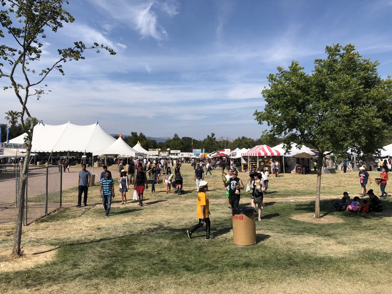 Visitors walking across the sunny Gilroy Garlic Festival grounds with white tents under blue sky