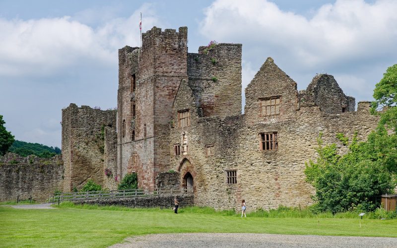 Ruined keep and walls of Ludlow Castle on a green lawn under a bright sky