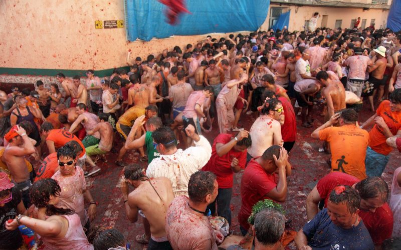 Crowd covered in tomato pulp in a narrow street during La Tomatina in Buñol