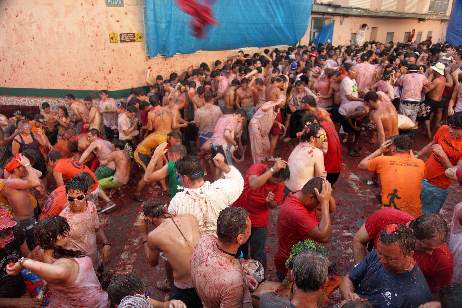 Crowd covered in tomato pulp in a narrow street during La Tomatina in Buñol