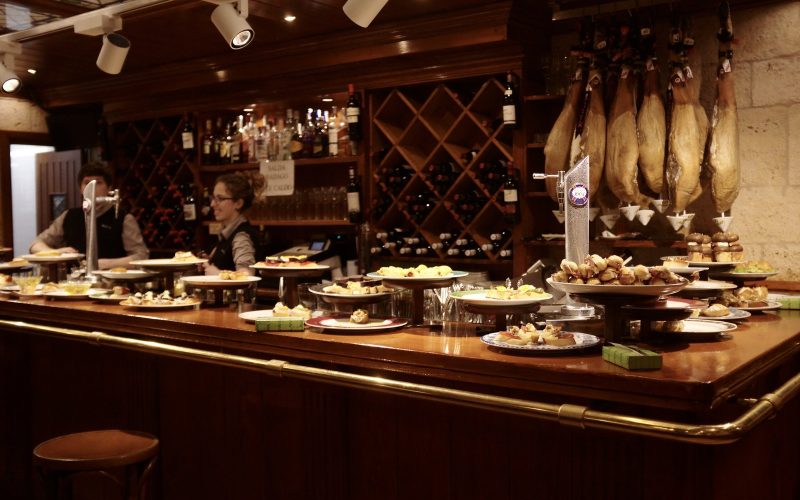 Pintxo bar counter with plates of pintxos and hanging hams in San Sebastián