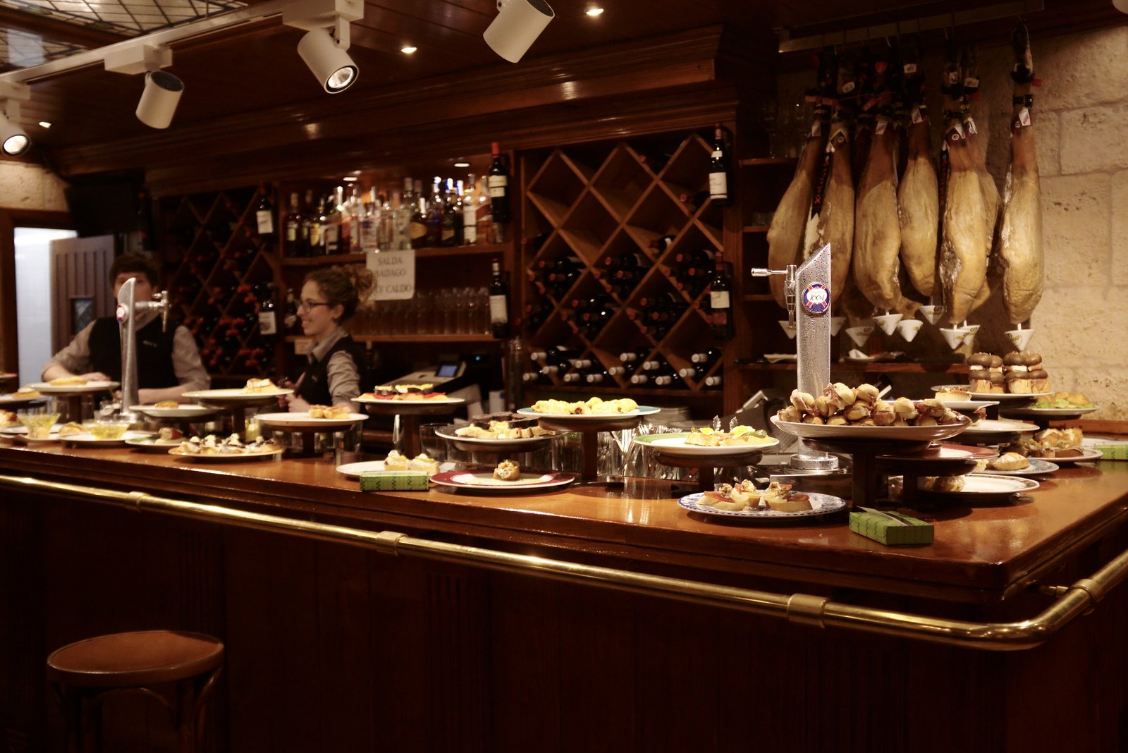 Pintxo bar counter with plates of pintxos and hanging hams in San Sebastián