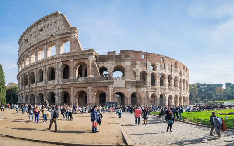 The Colosseum in Rome under a blue sky with visitors in the foreground