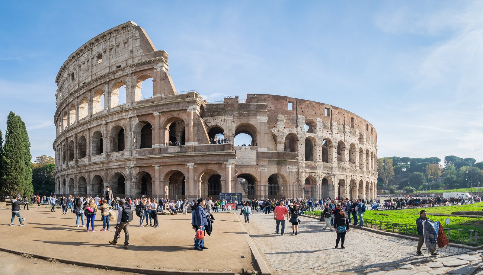 The Colosseum in Rome under a blue sky with visitors in the foreground