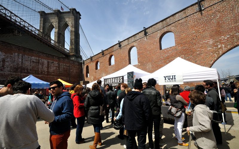 Smorgasburg food stalls and crowd beneath the Brooklyn Bridge in Dumbo