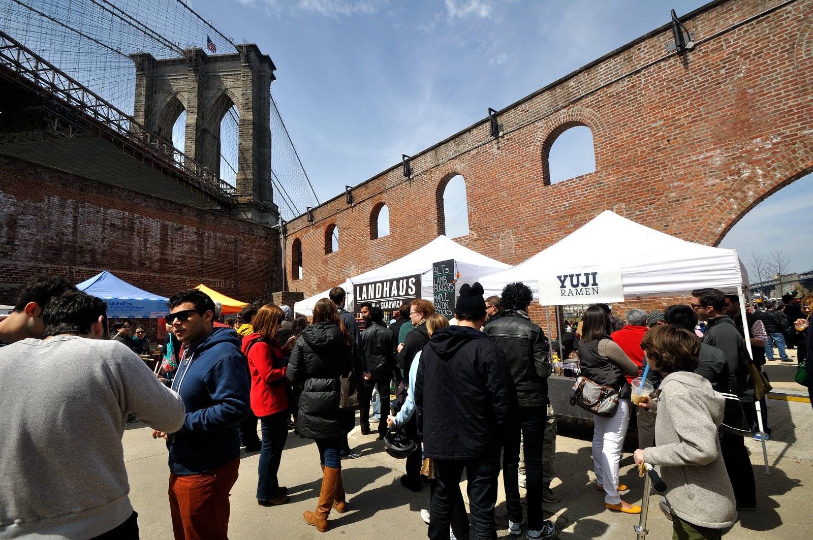 Smorgasburg food stalls and crowd beneath the Brooklyn Bridge in Dumbo
