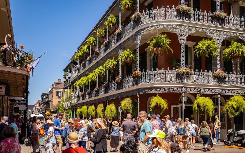 Lace-iron balconies with hanging ferns and a crowd on a French Quarter street corner