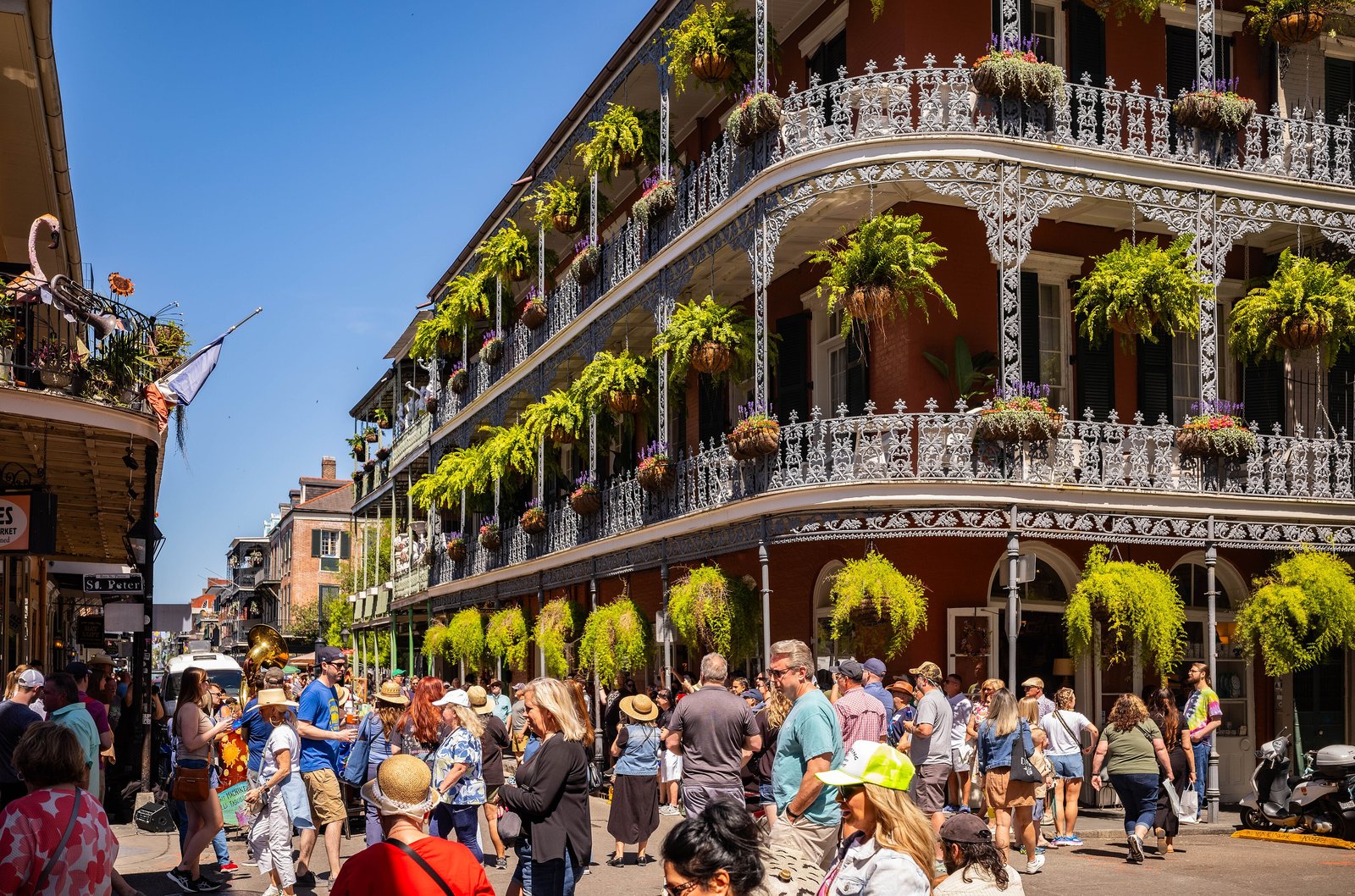 Lace-iron balconies with hanging ferns and a crowd on a French Quarter street corner