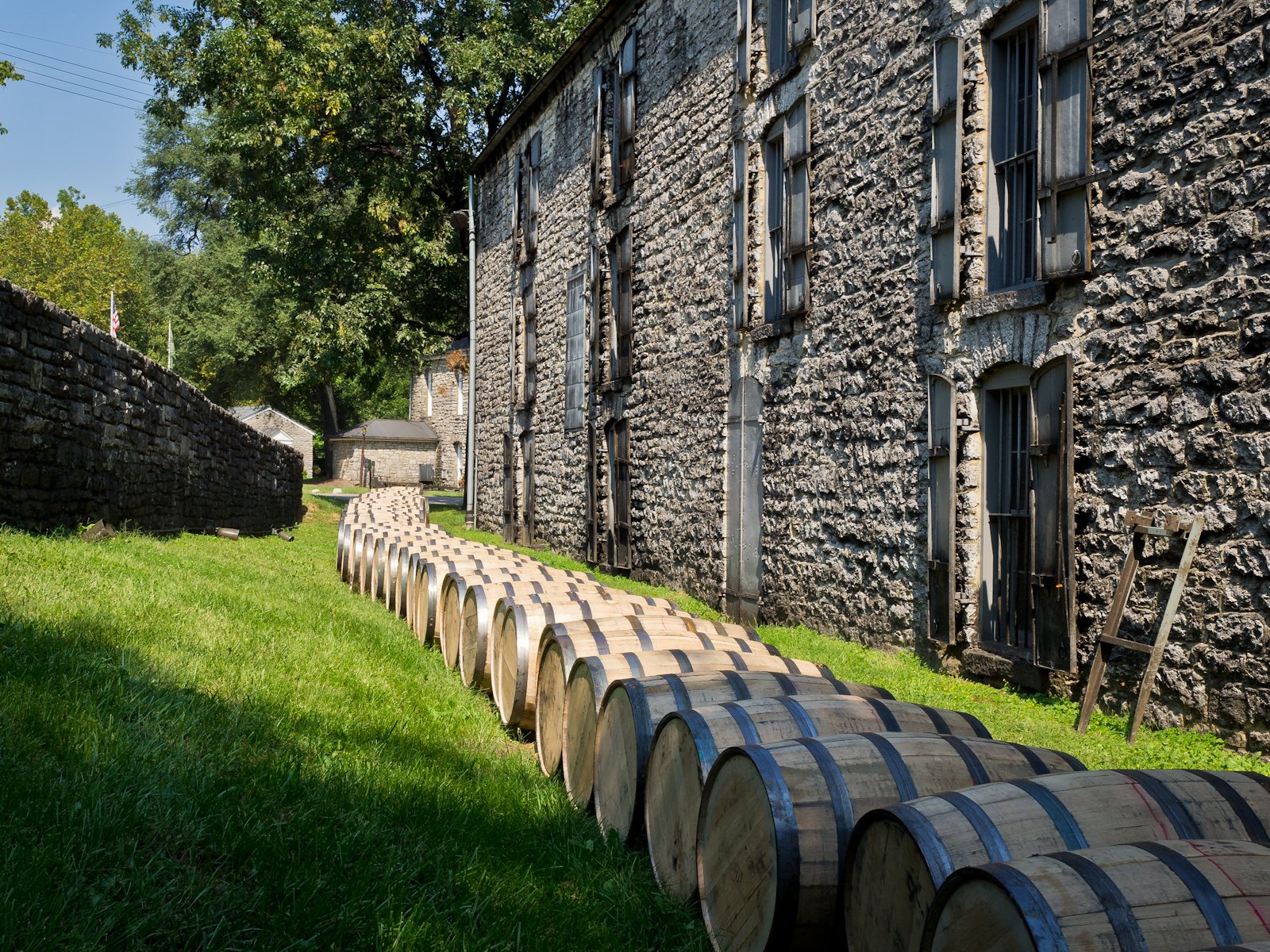 Bourbon barrels lined up on the grass beside a stone rickhouse at a Kentucky distillery