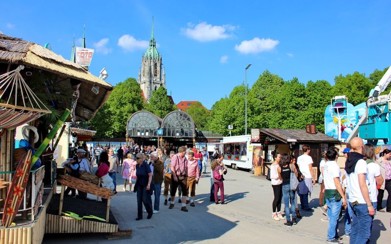 Visitors strolling the Frühlingsfest grounds with St Paul's church under a blue sky, Munich