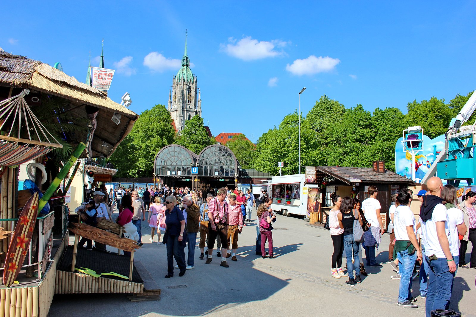 Visitors strolling the Frühlingsfest grounds with St Paul's church under a blue sky, Munich