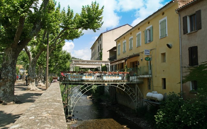Café terrace on a bridge over the river among plane trees in Collobrières