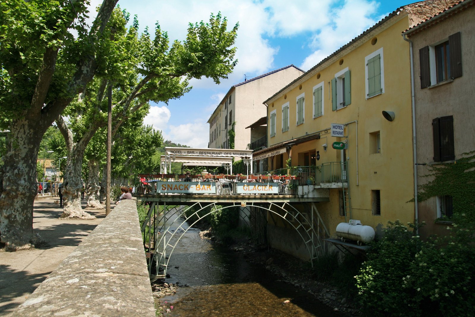Café terrace on a bridge over the river among plane trees in Collobrières
