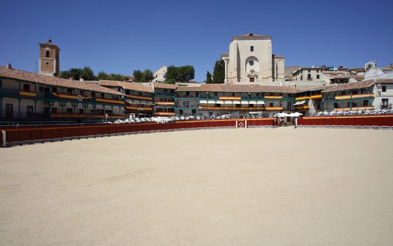Arcaded Plaza Mayor of Chinchón with green balconies under a blue sky