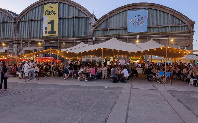 Diners on the central terrace under string lights in front of the Grandes Locos halls at dusk