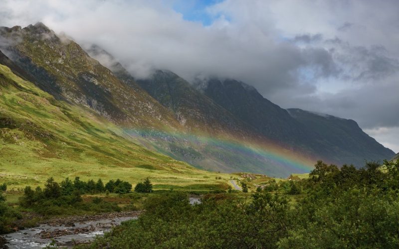 Rainbow over a green glen below misty mountains in Glen Coe, Scotland