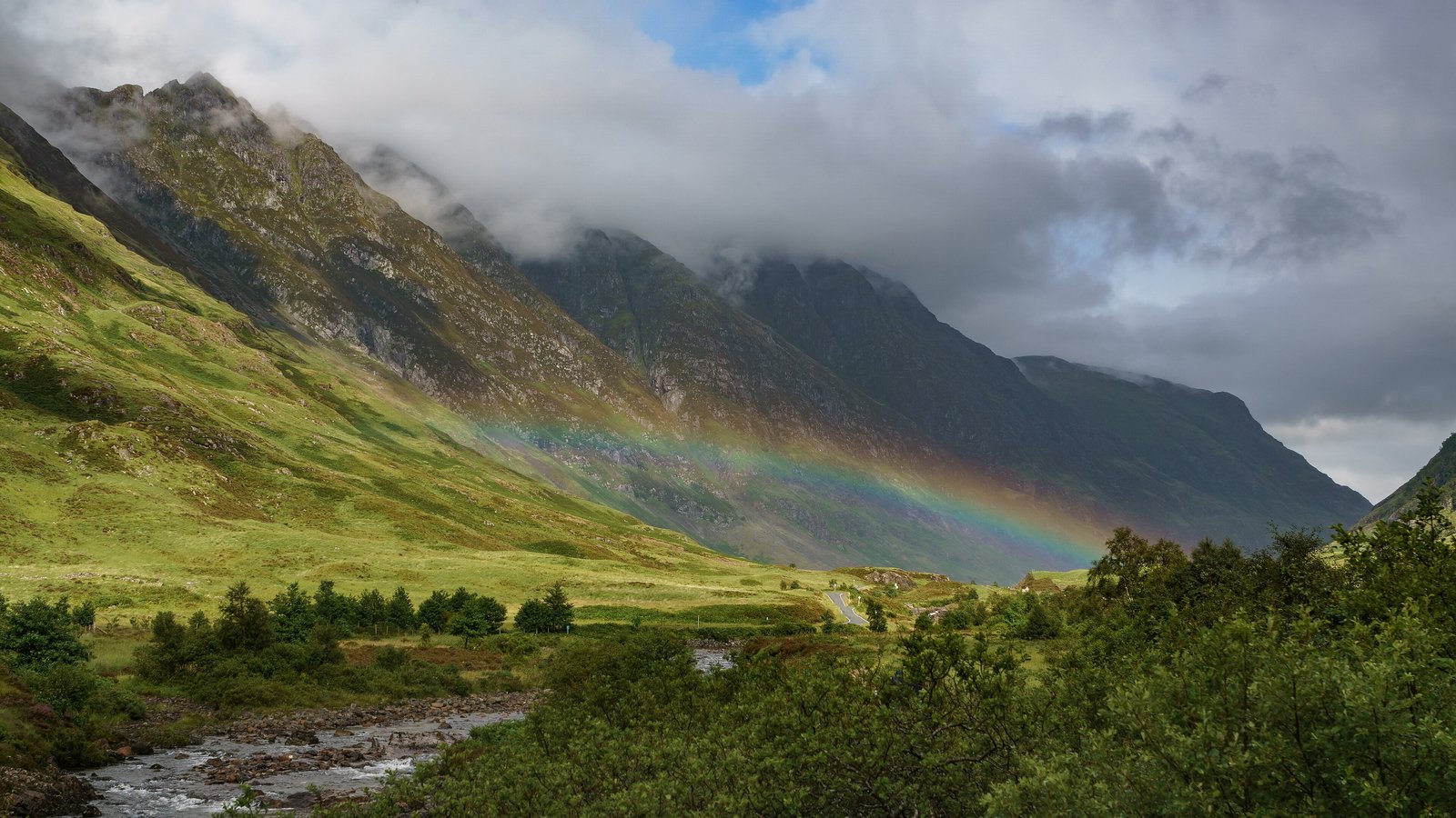 Rainbow over a green glen below misty mountains in Glen Coe, Scotland