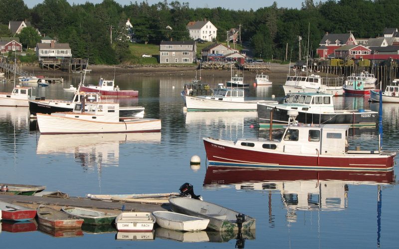 Lobster boats moored in a calm Maine harbor with waterfront houses behind